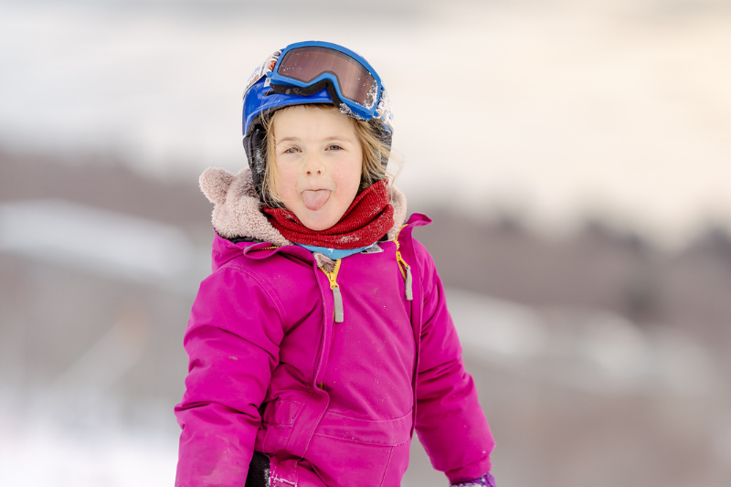 Enfant en combinaison rose fait une grimace sur une piste de ski.