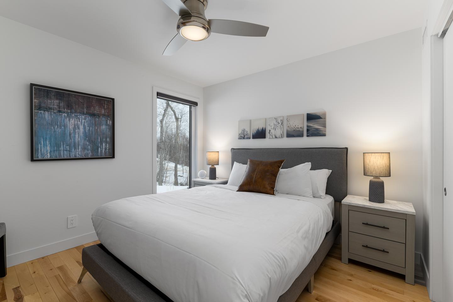 Chambre moderne avec lit double, tableaux, lampes et fenêtre ouverte sur l'extérieur enneigé.