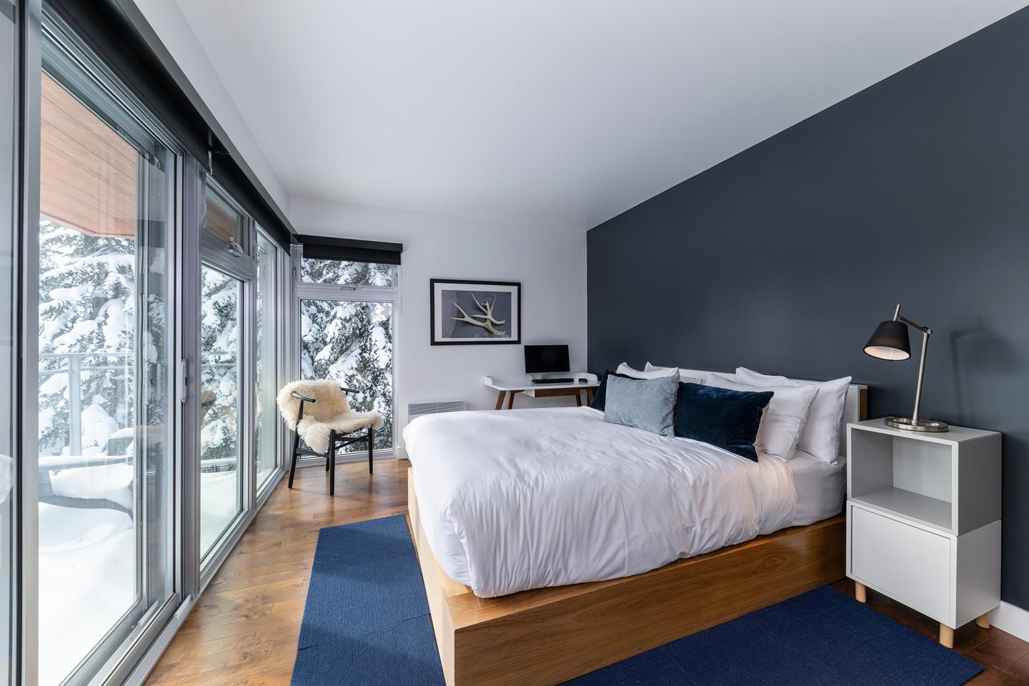 Chambre moderne avec lit double, mur bleu, grande fenêtre et vue sur la neige.