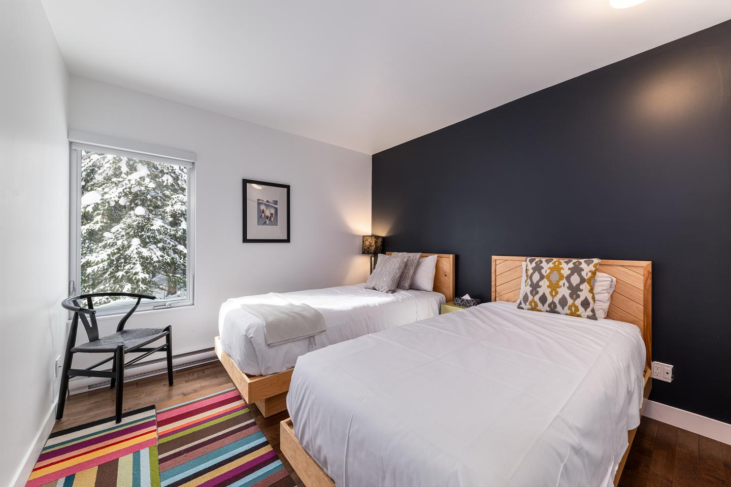 Deux lits dans une chambre moderne avec un mur noir, tapis rayé et chaise noire.