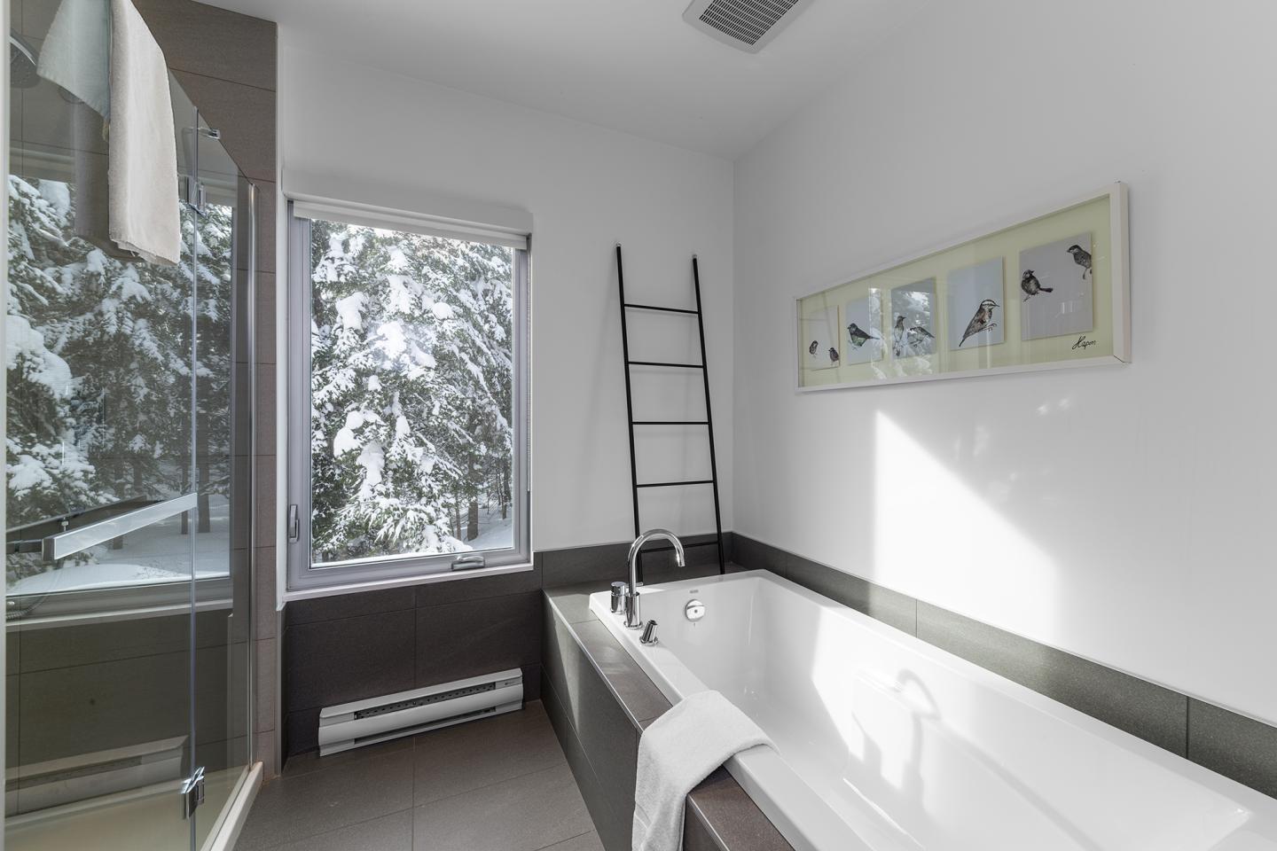 Salle de bain moderne avec baignoire, fenêtre enneigée, et échelle décorative.