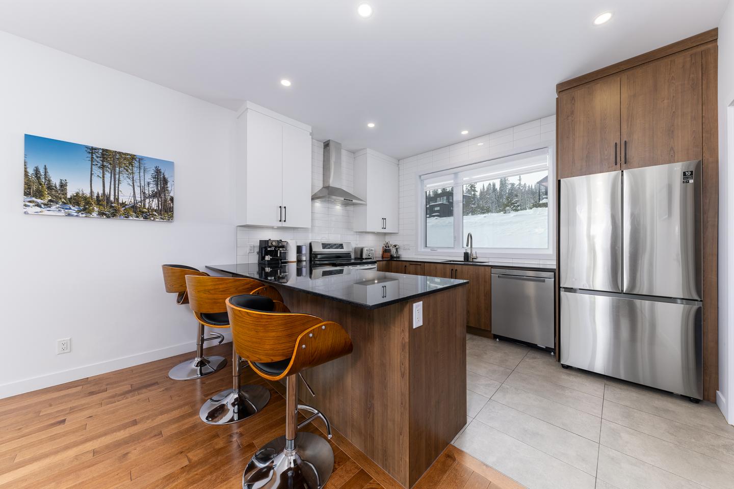 Cuisine moderne avec comptoir en bois, tabourets, et électroménagers en acier inoxydable.