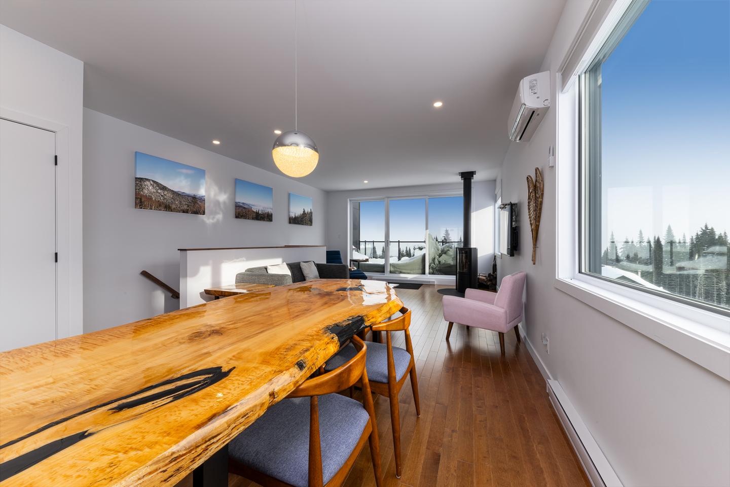 Salle à manger moderne avec grande table en bois, fenêtres lumineuses.