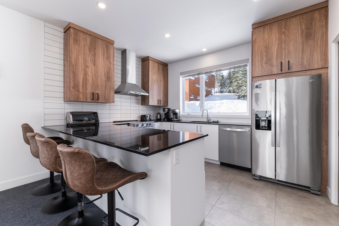 Cuisine moderne avec comptoir en granite, tabourets, frigo en inox et armoires en bois brun.