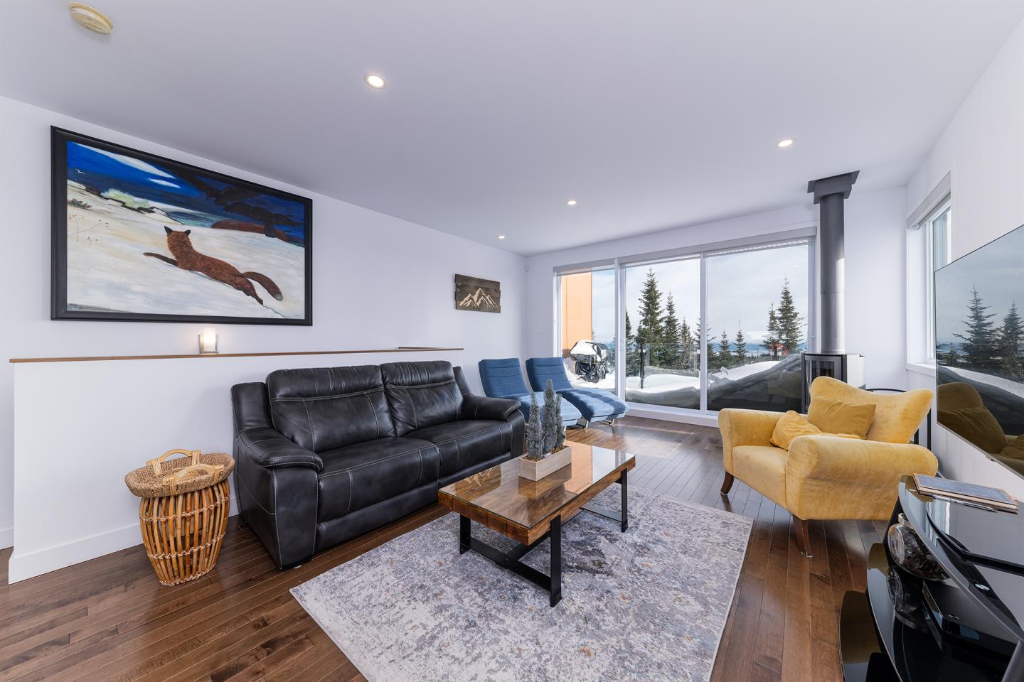 Salon moderne avec canapé noir, fauteuils colorés, et vue sur la montagne enneigée.