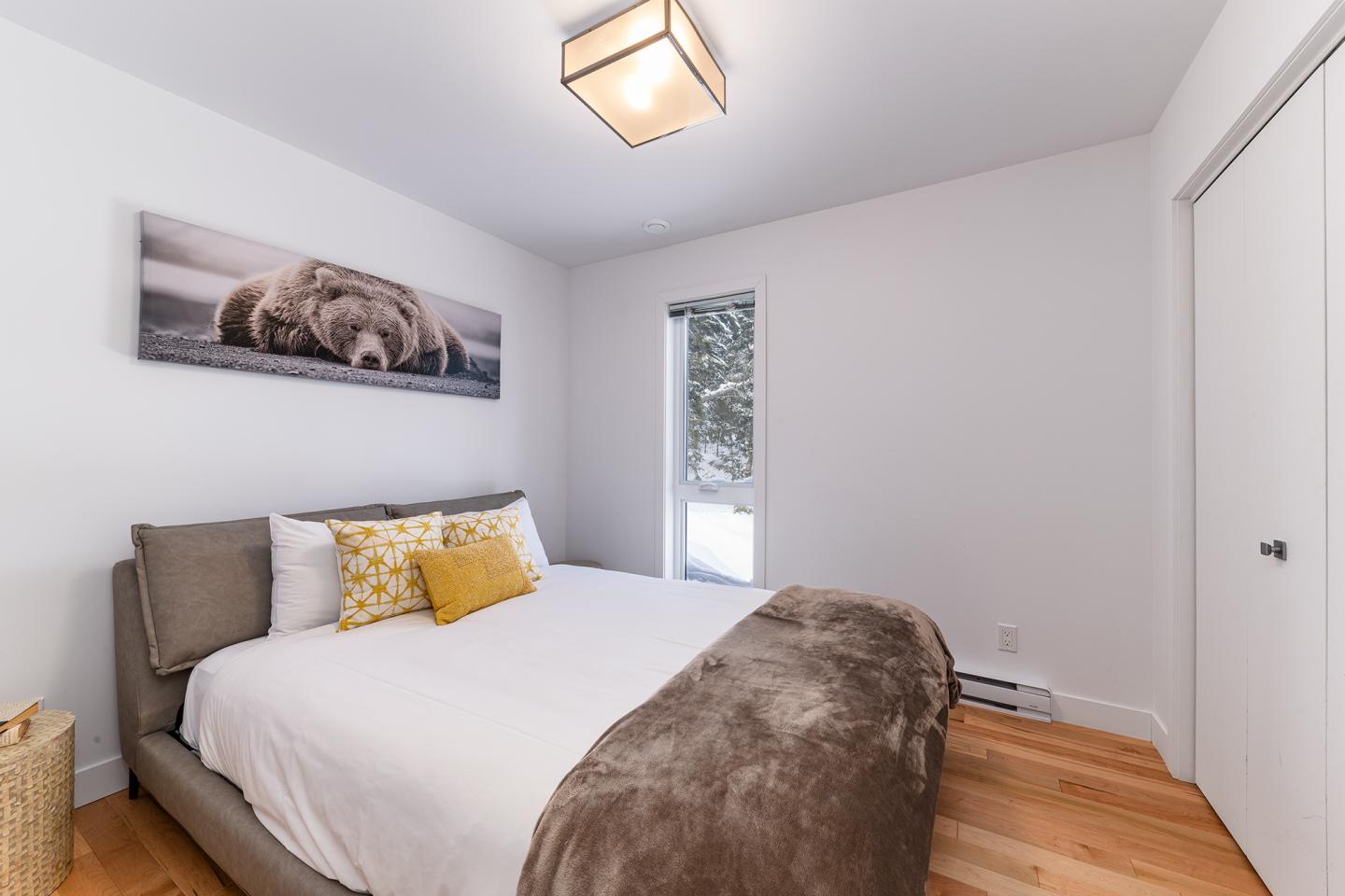 Chambre moderne avec grand lit, photo d'ours au-dessus, parquet clair.