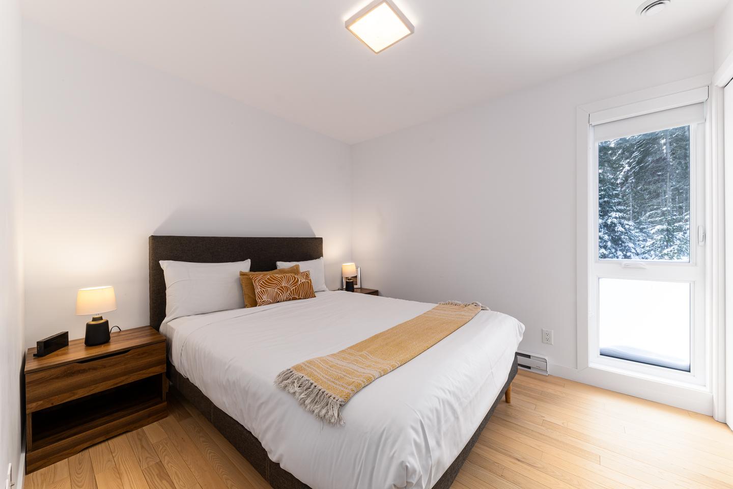 Chambre lumineuse avec lit double, murs blancs, vue sur l'extérieur enneigé.