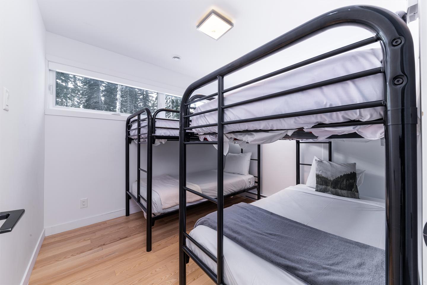 Chambre claire avec deux lits superposés noirs, parquet en bois.