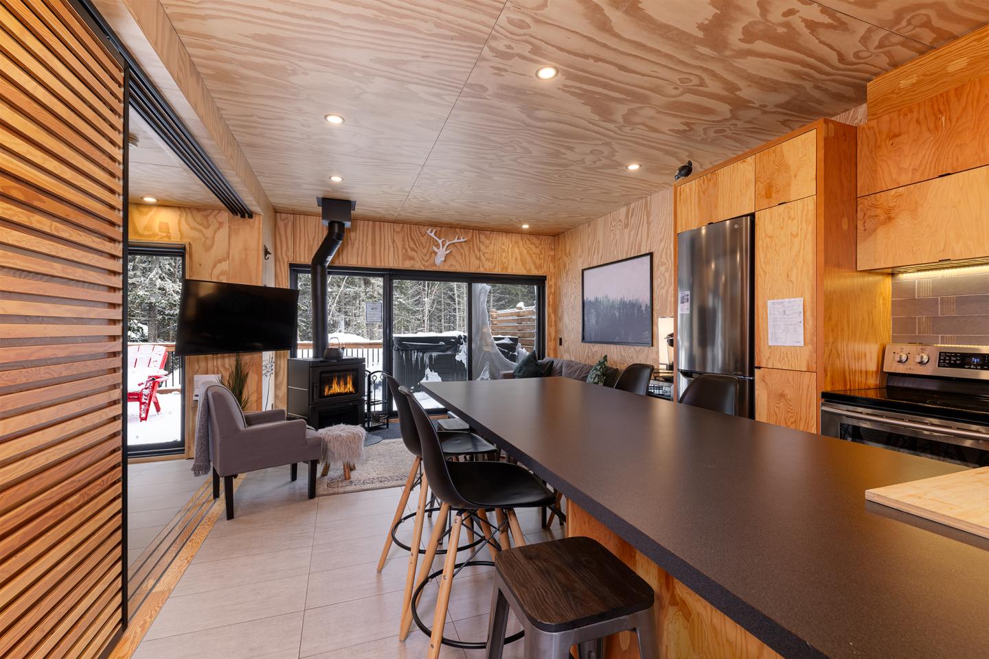 Cuisine moderne en bois, avec îlot noir et grandes fenêtres sur un paysage enneigé.