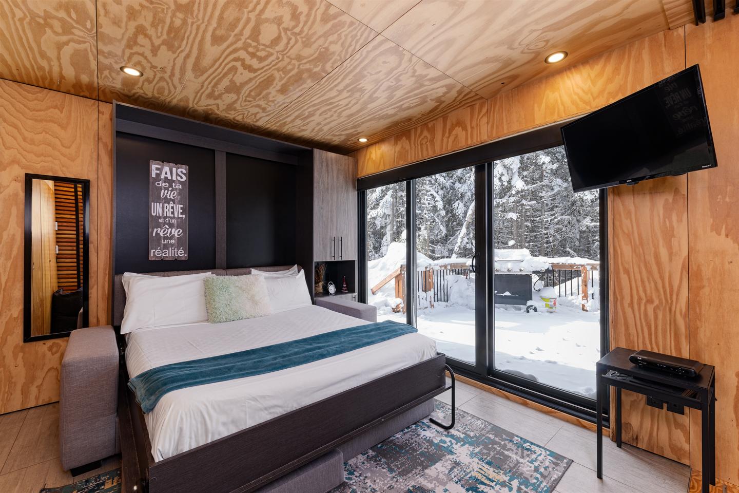 Chambre moderne en bois avec lit double, grande fenêtre donnant sur la neige.