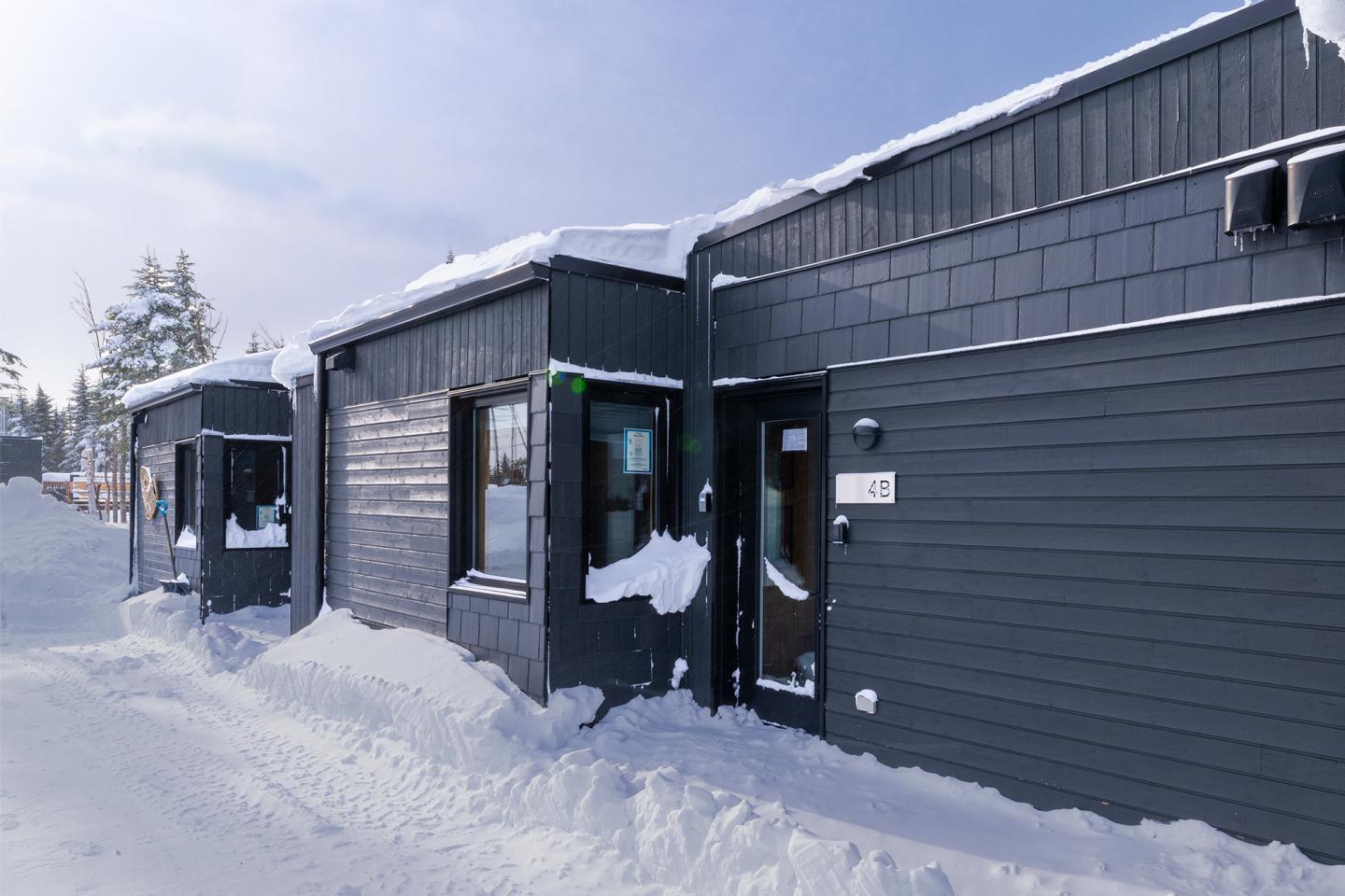 Bâtiments noirs dans la neige, ciel clair.