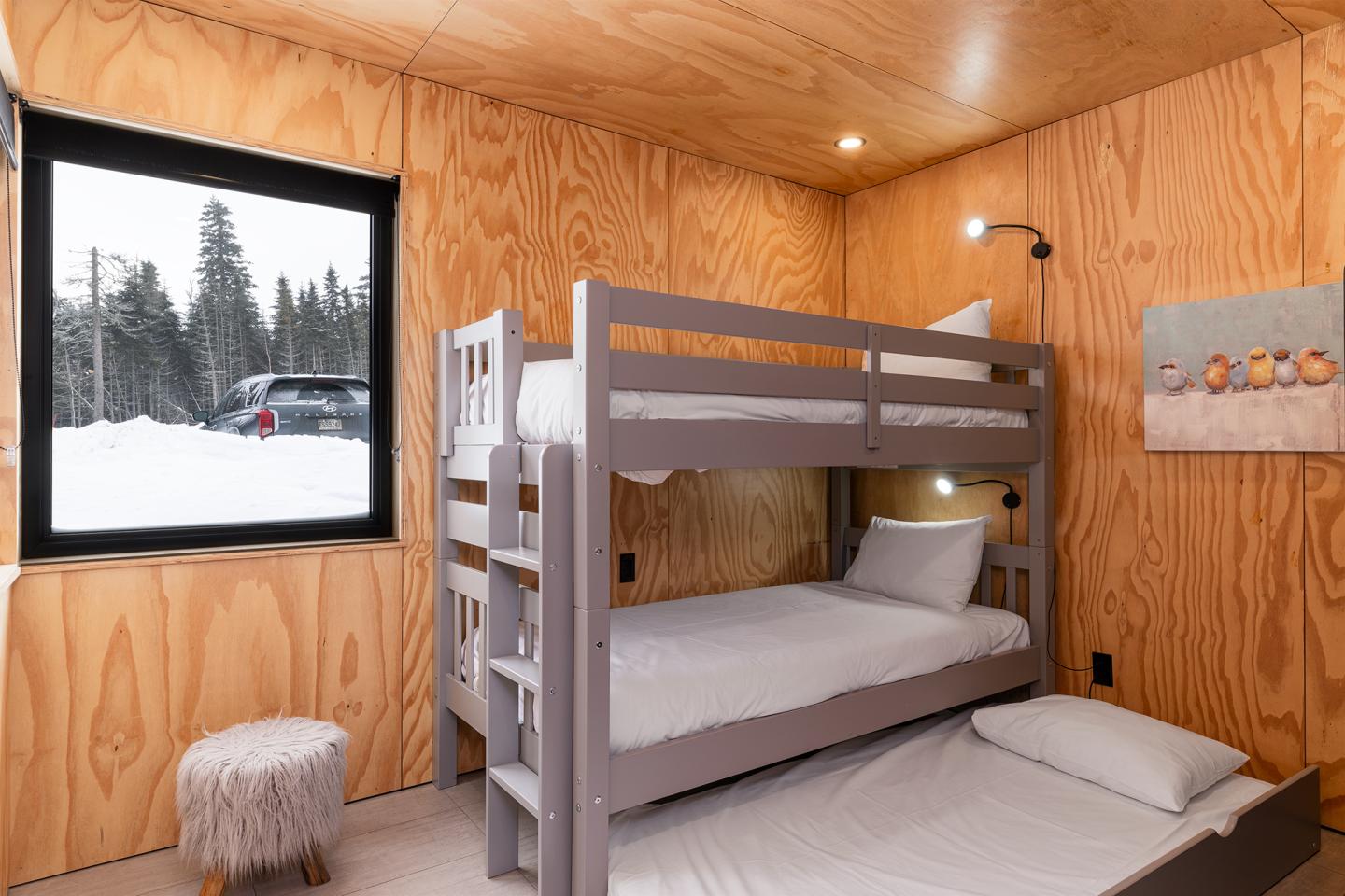 Chambre en bois clair avec lits superposés et fenêtre sur paysage enneigé.