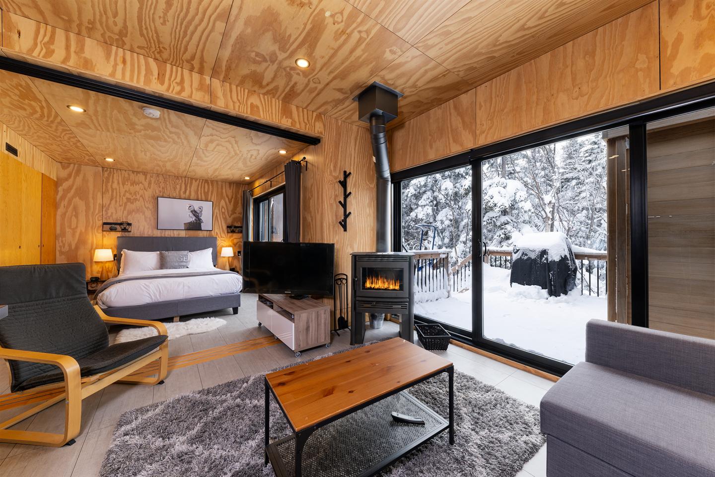 Intérieur d'un chalet en bois, chaleureux avec vue sur neige par de grandes fenêtres.