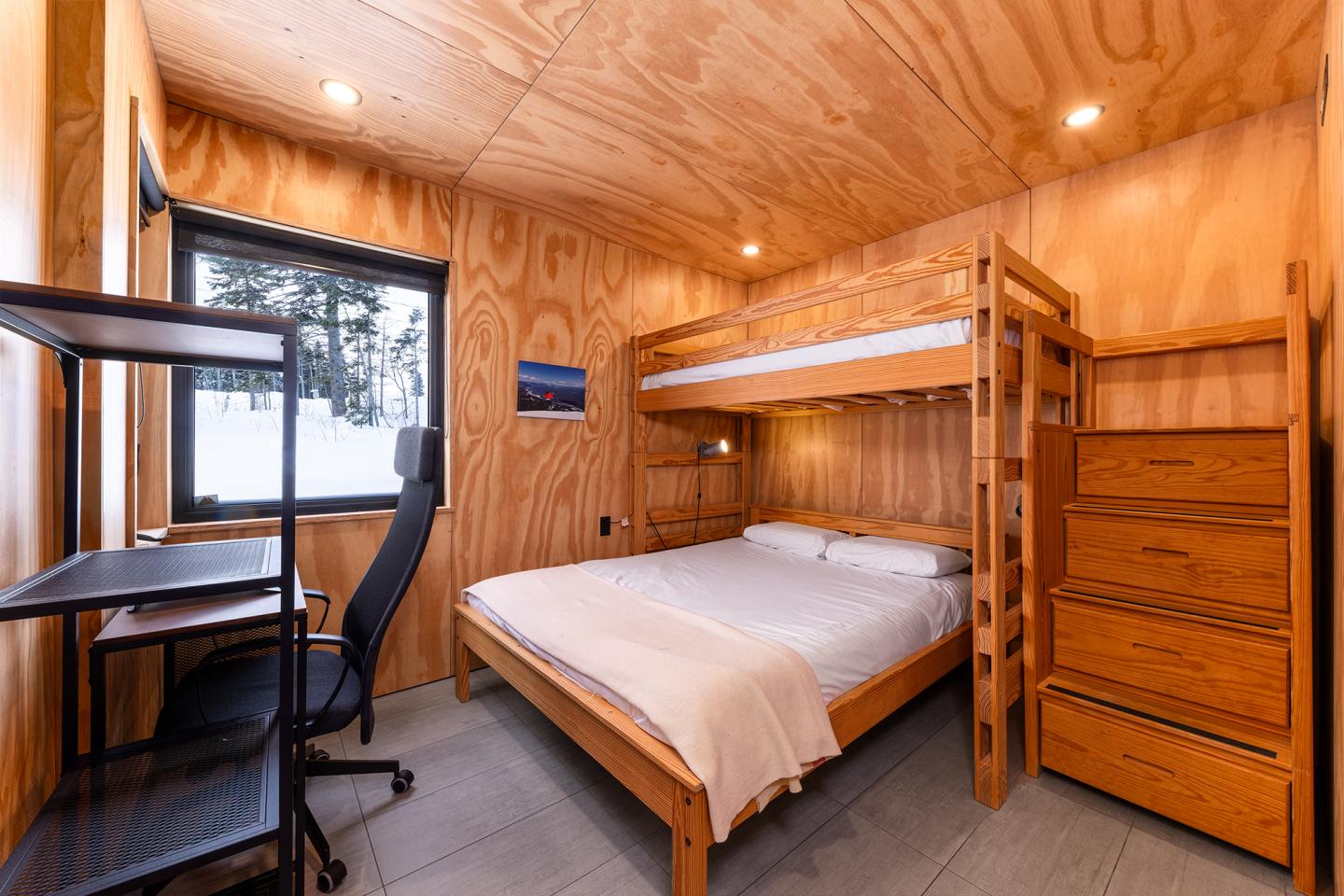 Petite chambre en bois avec lit superposé, bureau et fenêtre donnant sur l'extérieur.