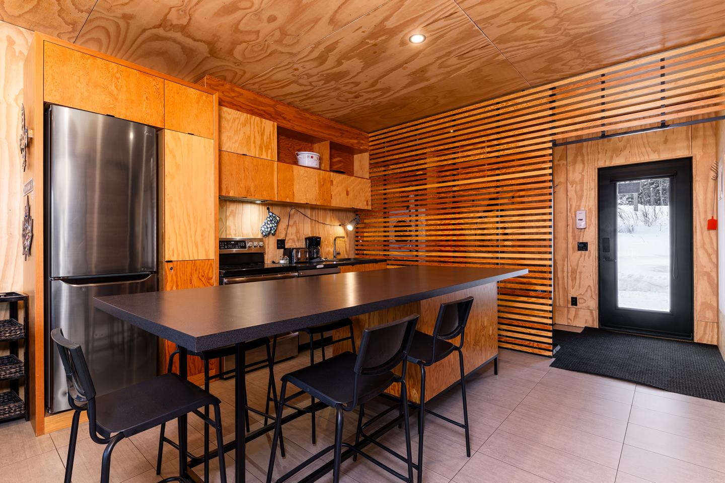 Cuisine moderne en bois avec un îlot central et des chaises noires.