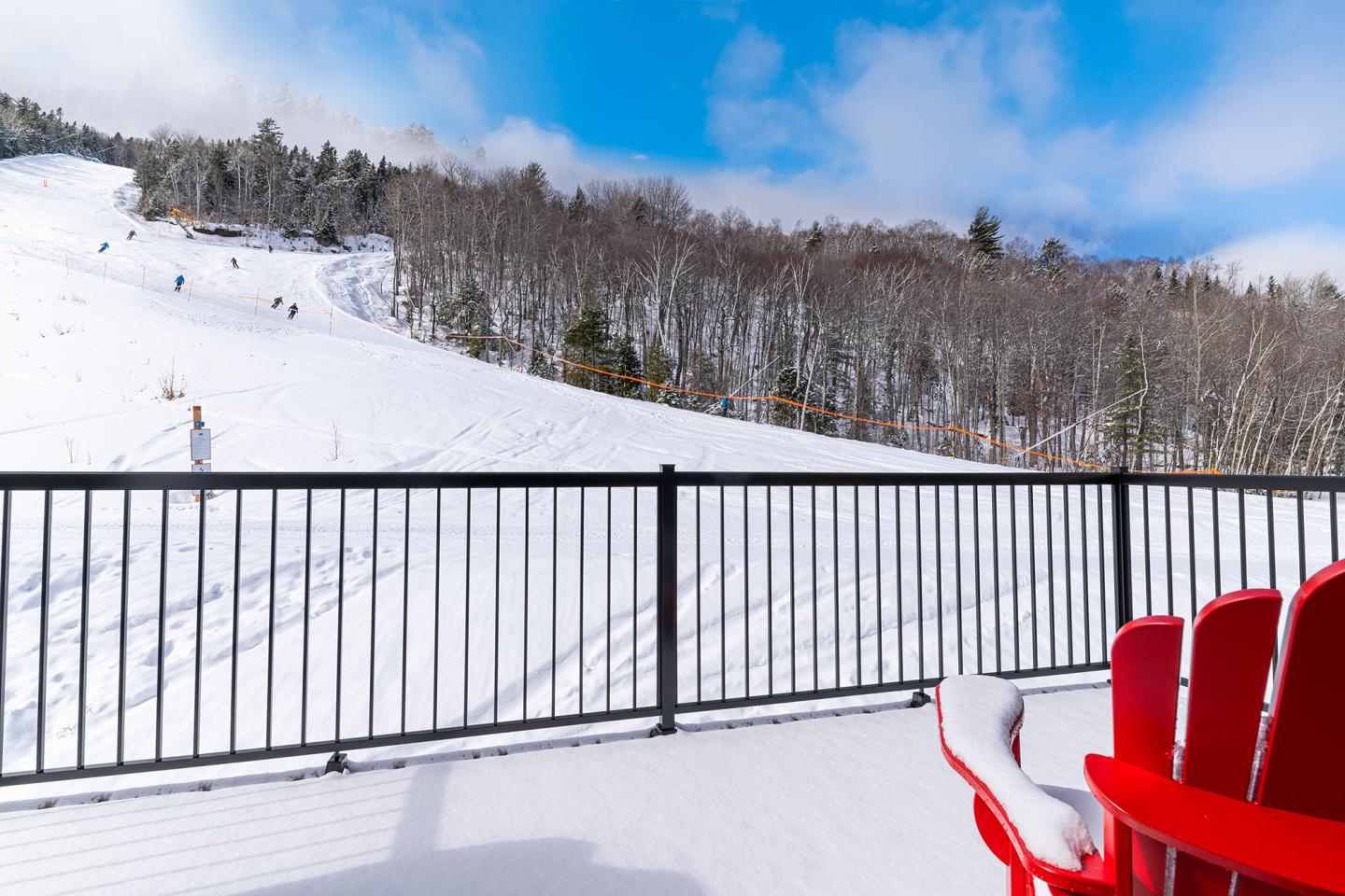 Terrasse enneigée avec vue sur piste de ski, ciel bleu, chaises rouges.