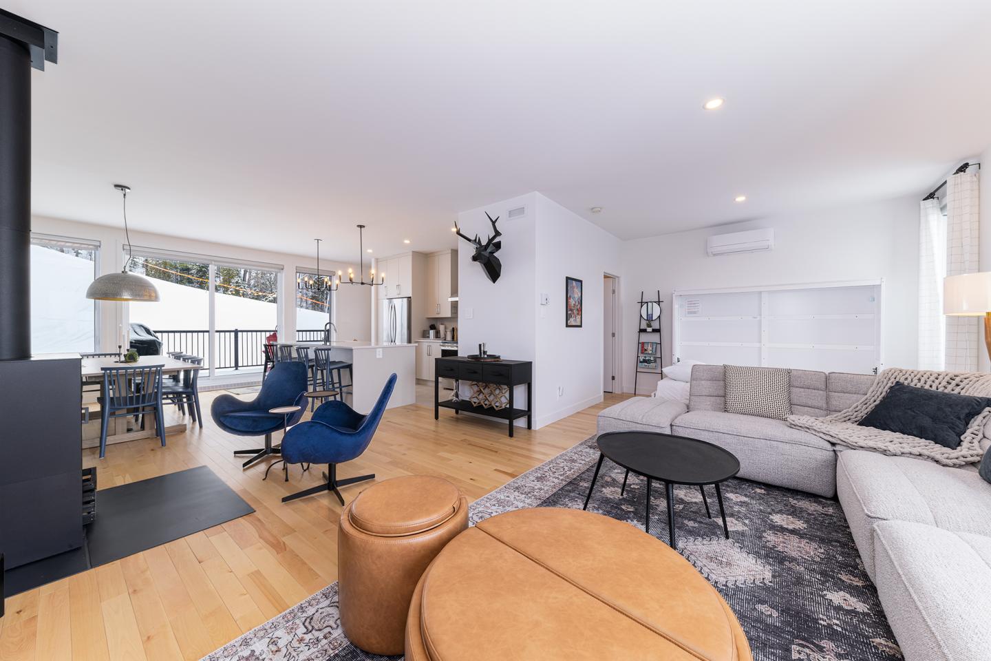 Salon moderne, canapé gris, chaises bleues, tables rondes, intérieur lumineux.