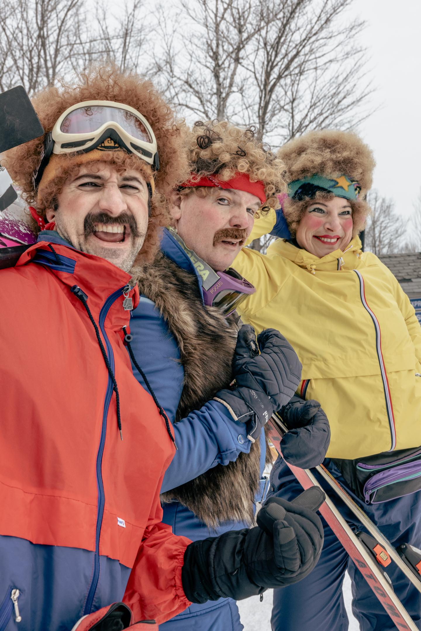 Trois personnes souriantes en tenue de ski colorée, avec des bonnets en fourrure.