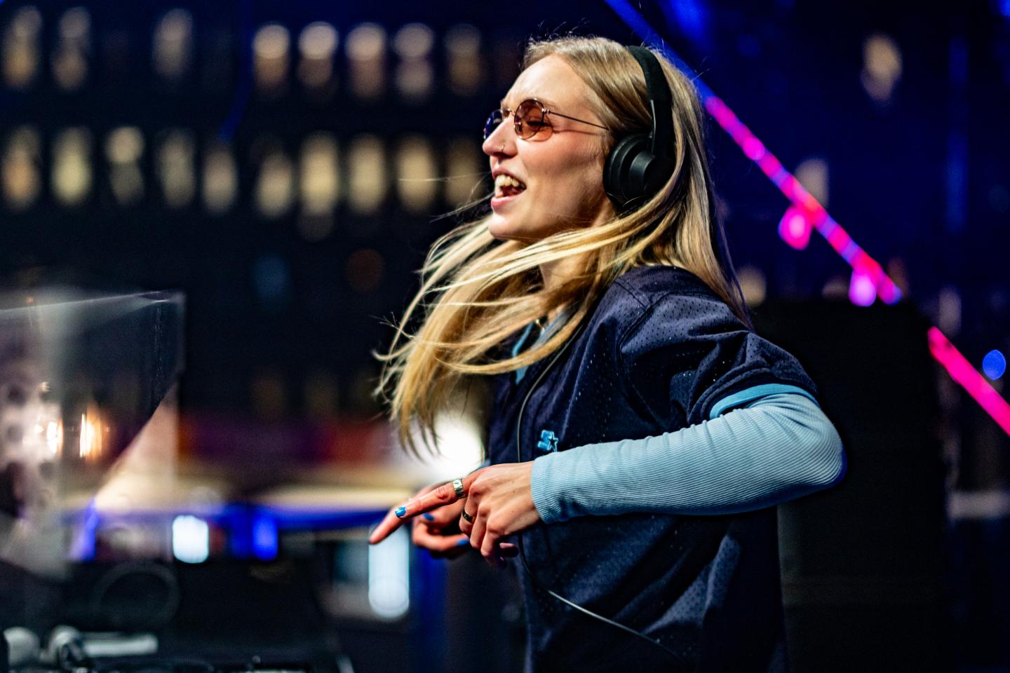 DJ souriant avec casque sur les oreilles, éclairage coloré en arrière-plan.