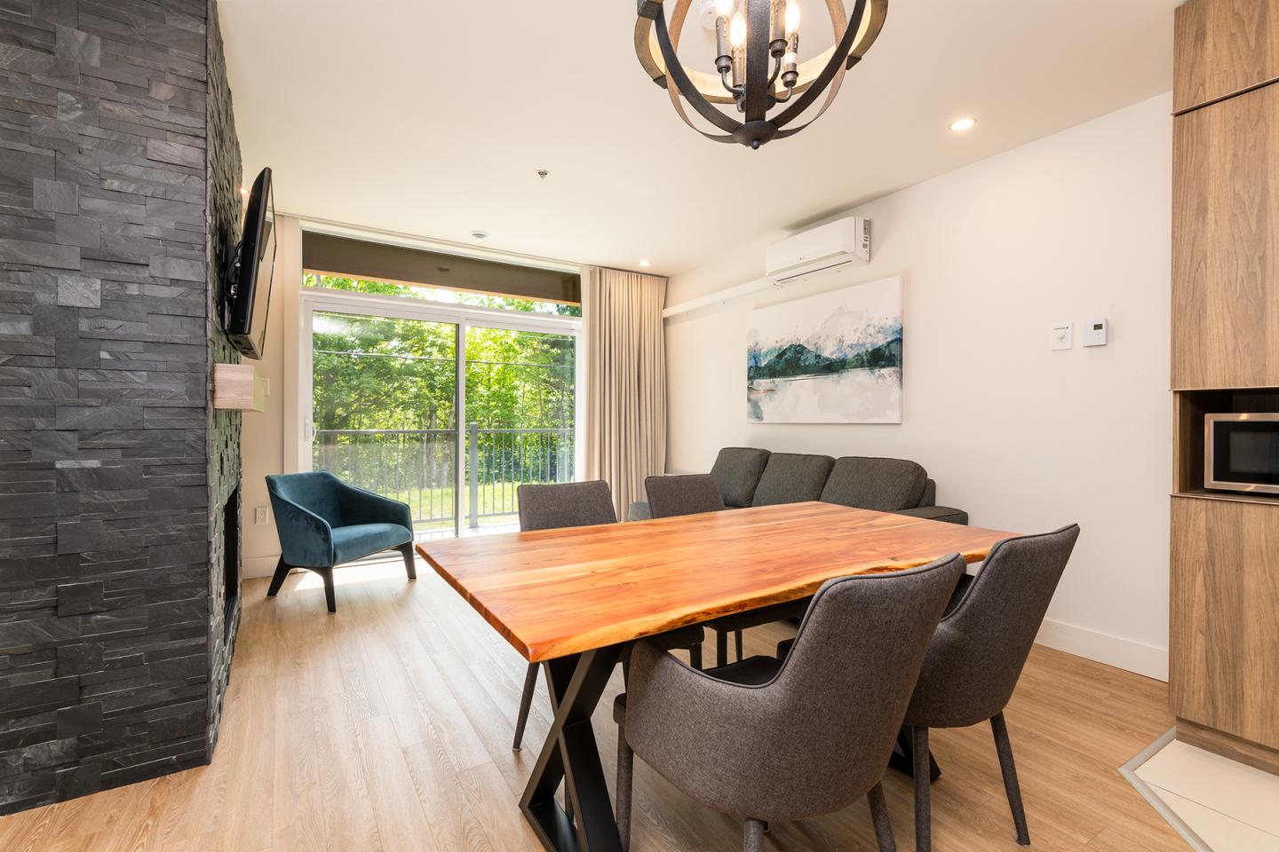 Salle à manger moderne avec table en bois, chaises grises et baie vitrée.