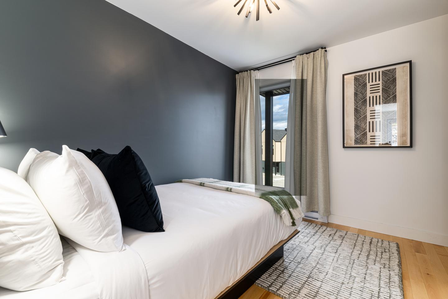 Chambre moderne avec mur gris, lit blanc et fenêtre.