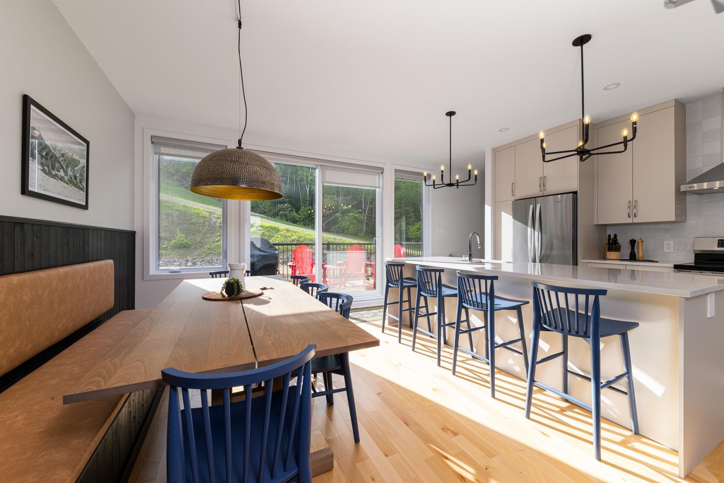 Cuisine moderne lumineuse avec îlot central, chaises bleues et grande table en bois.