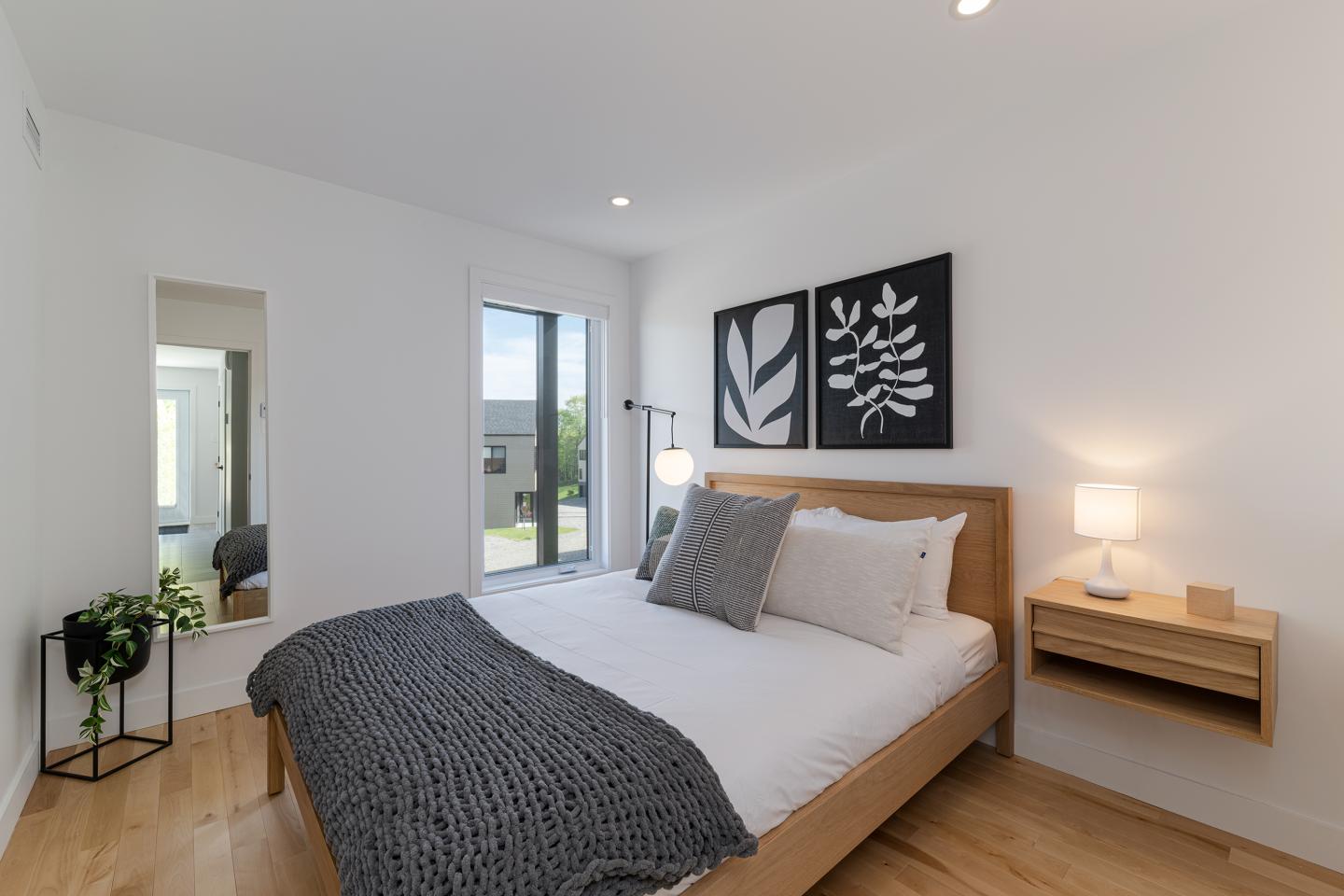 Chambre moderne avec lit double, décorations murales en noir et blanc, lampe de chevet allumée.