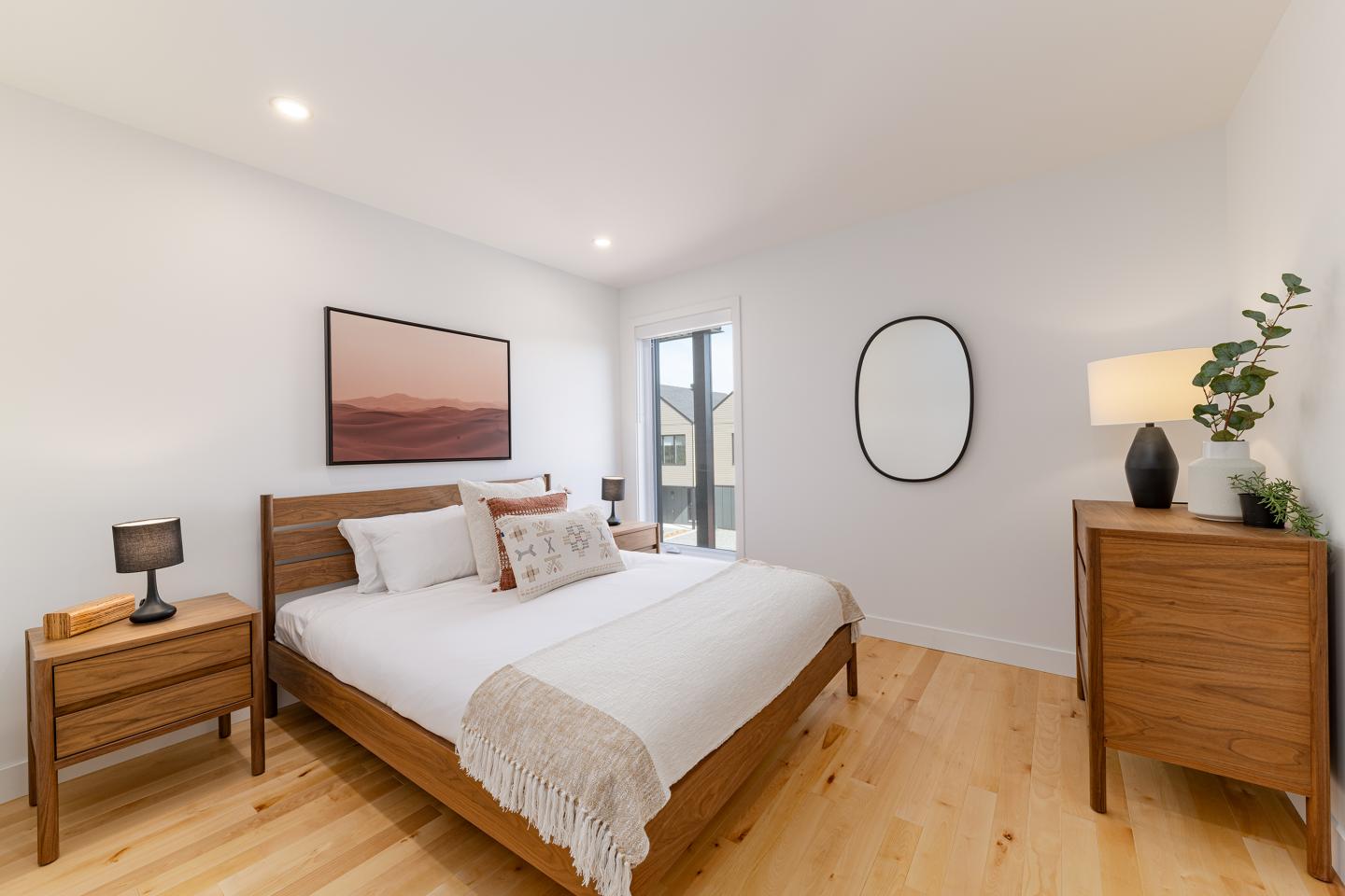 Chambre moderne avec lit double, meubles en bois, tableau et miroir ovale.