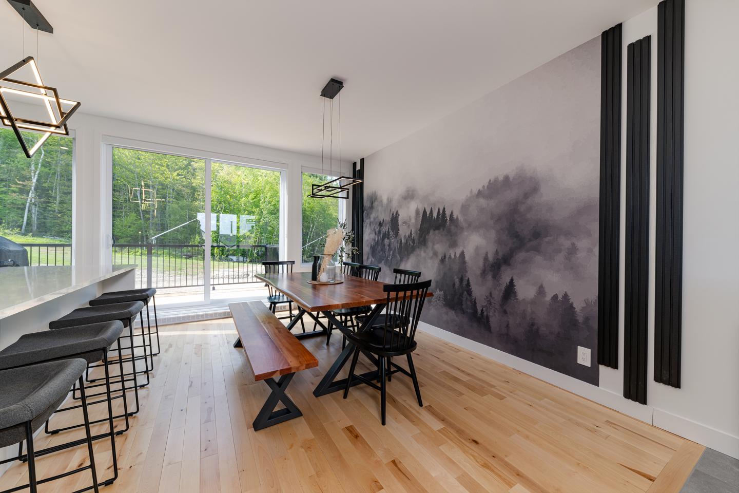 Salle à manger moderne avec table en bois, mur décoratif, fenêtres donnant sur un jardin.