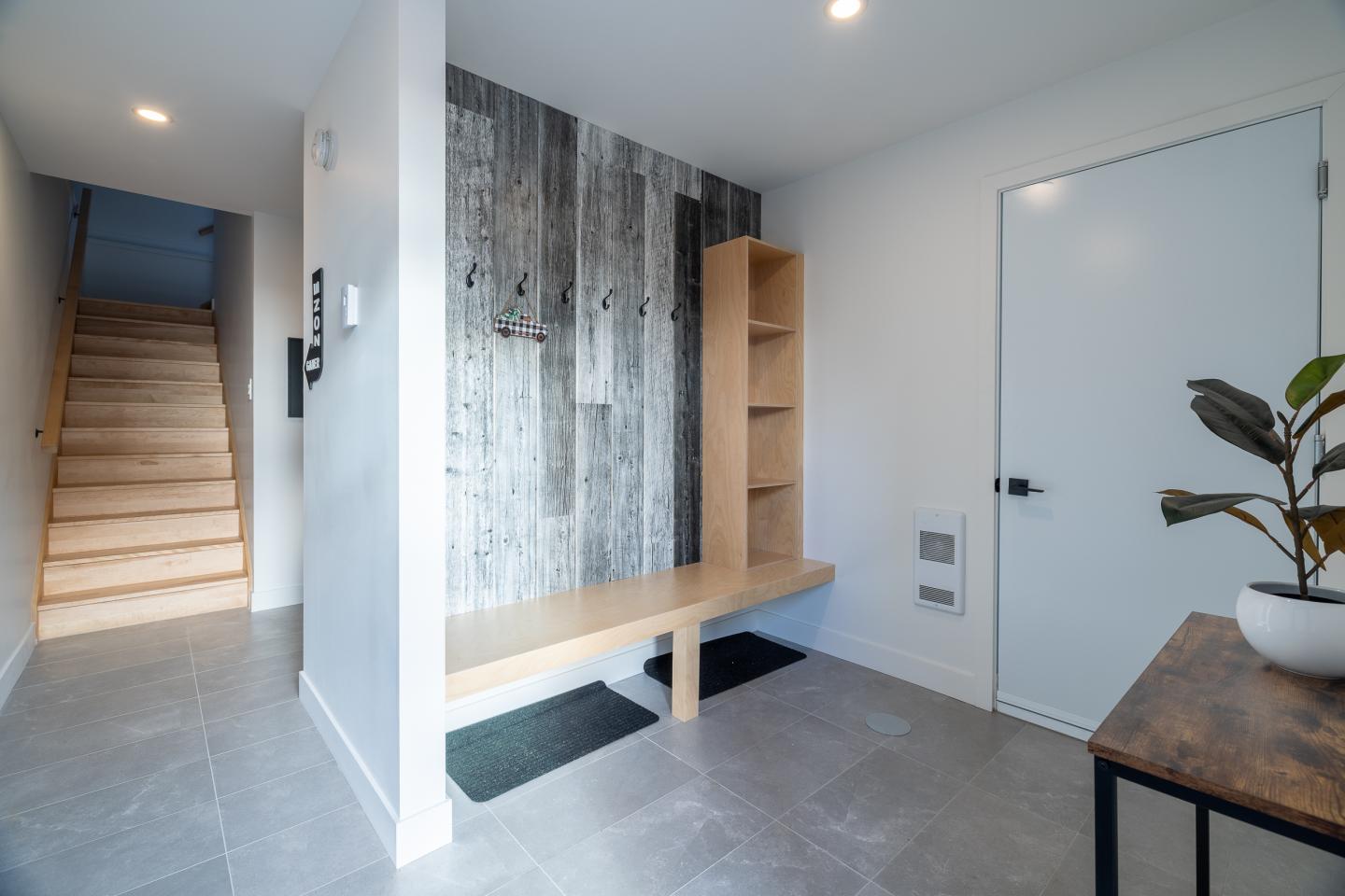Entrée moderne avec banc en bois, mur texturé, et escalier sur la gauche.