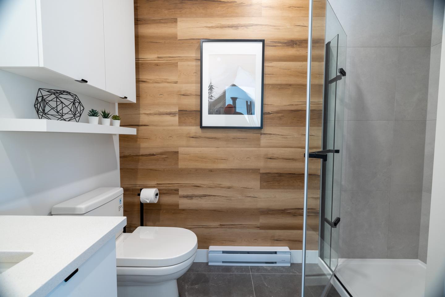 Salle de bain moderne avec douche en verre, mur en bois et étagères blanches.