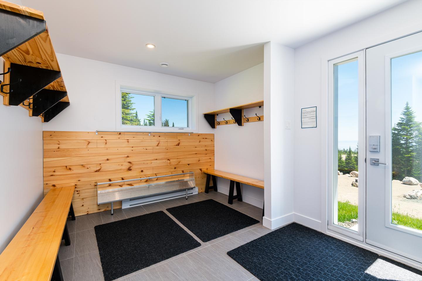 Vestiaire lumineux avec bancs en bois, étagères noires, vue extérieure sur des arbres.