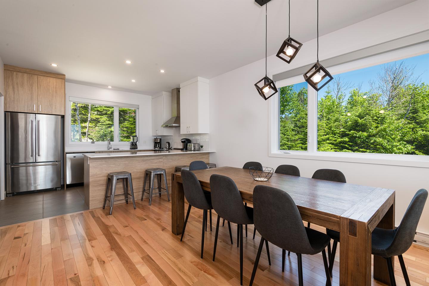 Cuisine moderne avec table en bois, chaises noires, et fenêtre sur jardin.
