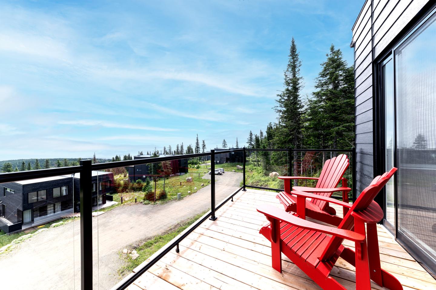 Deux chaises rouges sur une terrasse en bois avec vue sur forêt et ciel bleu.