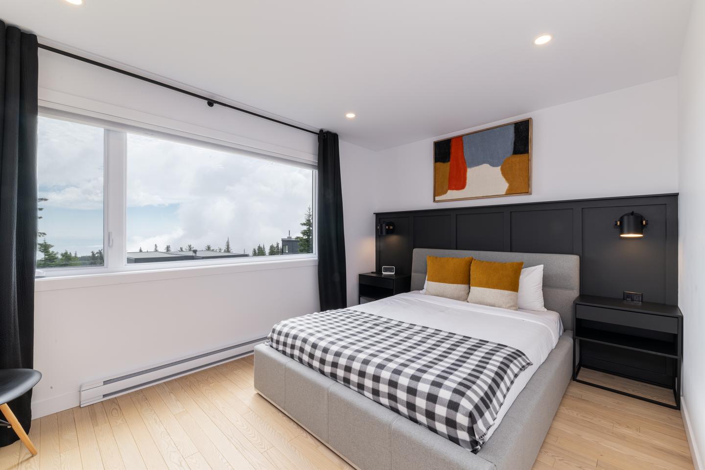 Chambre moderne avec lit double, plaid à carreaux, et vue sur la nature.