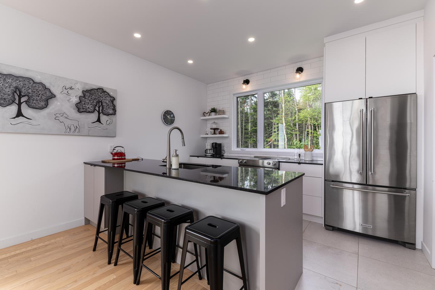 Cuisine moderne avec îlot central, tabourets noirs et grandes fenêtres.