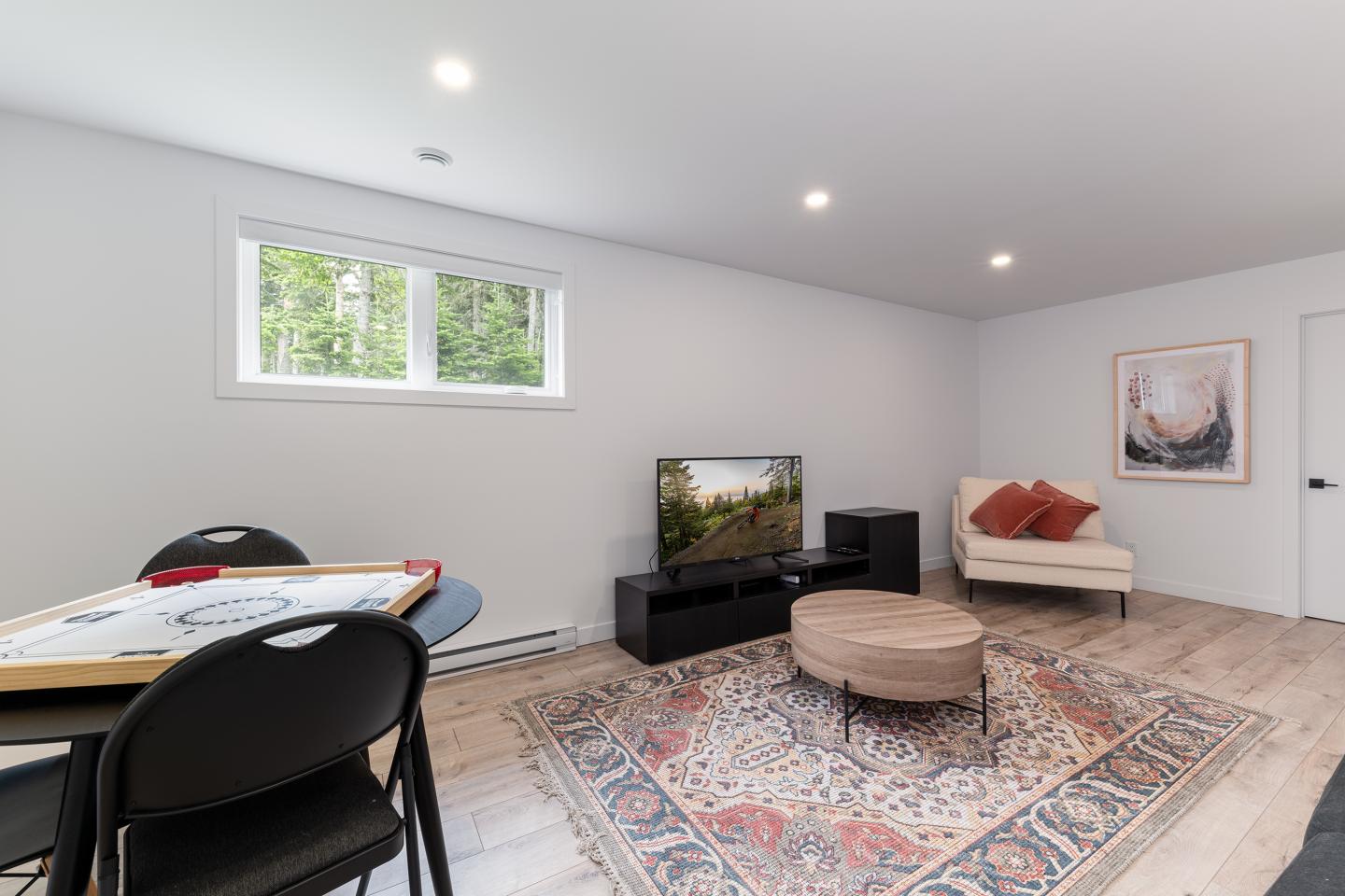 Salon moderne avec canapé blanc, table basse, tapis coloré et télévision.