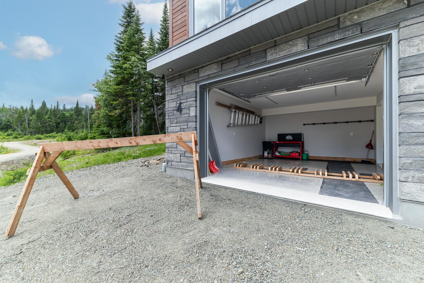 Garage ouvert avec des outils à l'intérieur, entouré d'arbres et d'un ciel bleu.