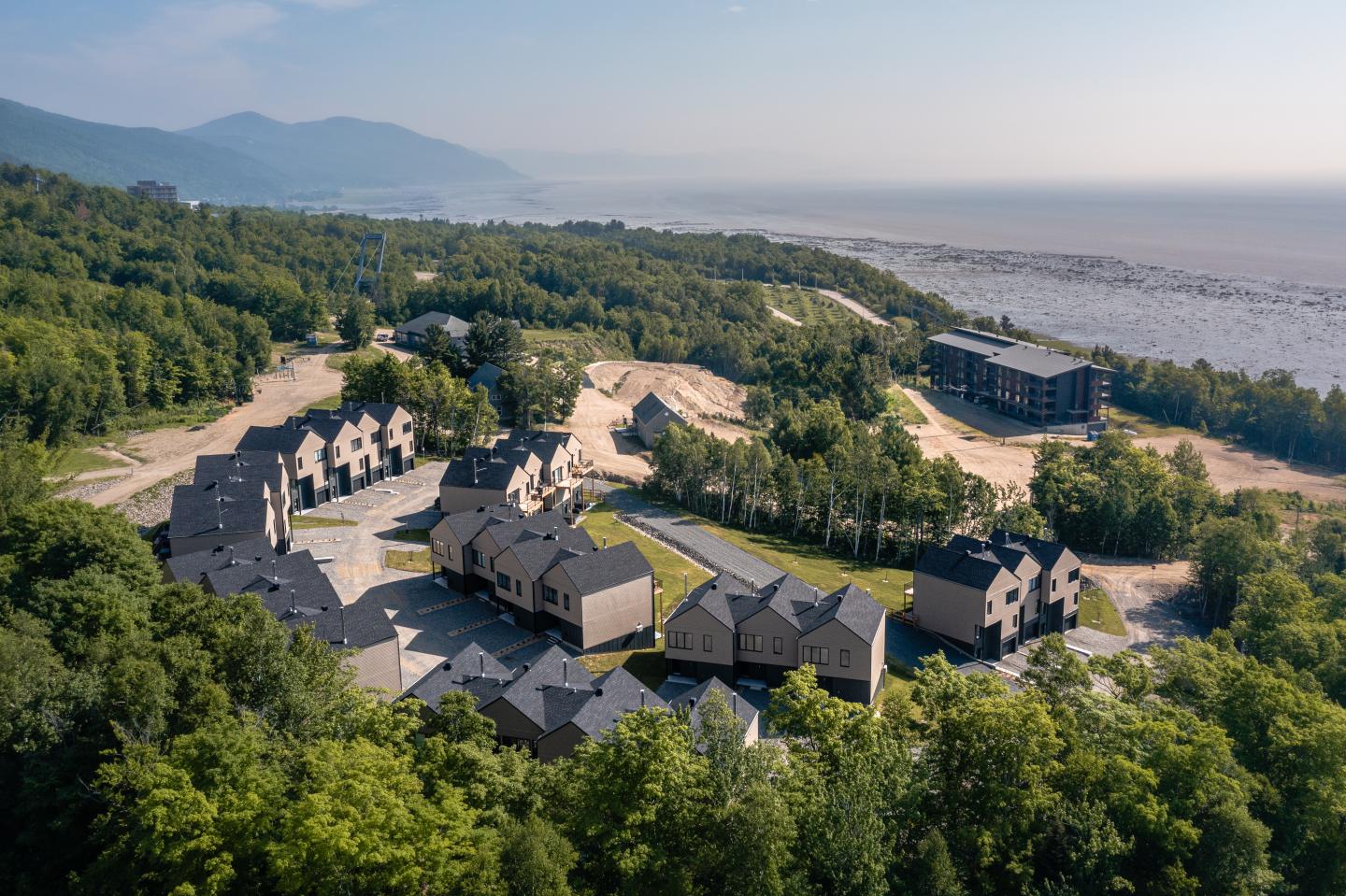 Village côtier entouré de forêts et montagnes, plage à l'horizon.