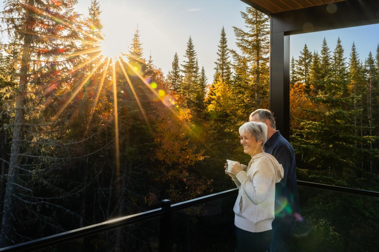 Un couple âgé admire le coucher de soleil depuis une terrasse boisée.