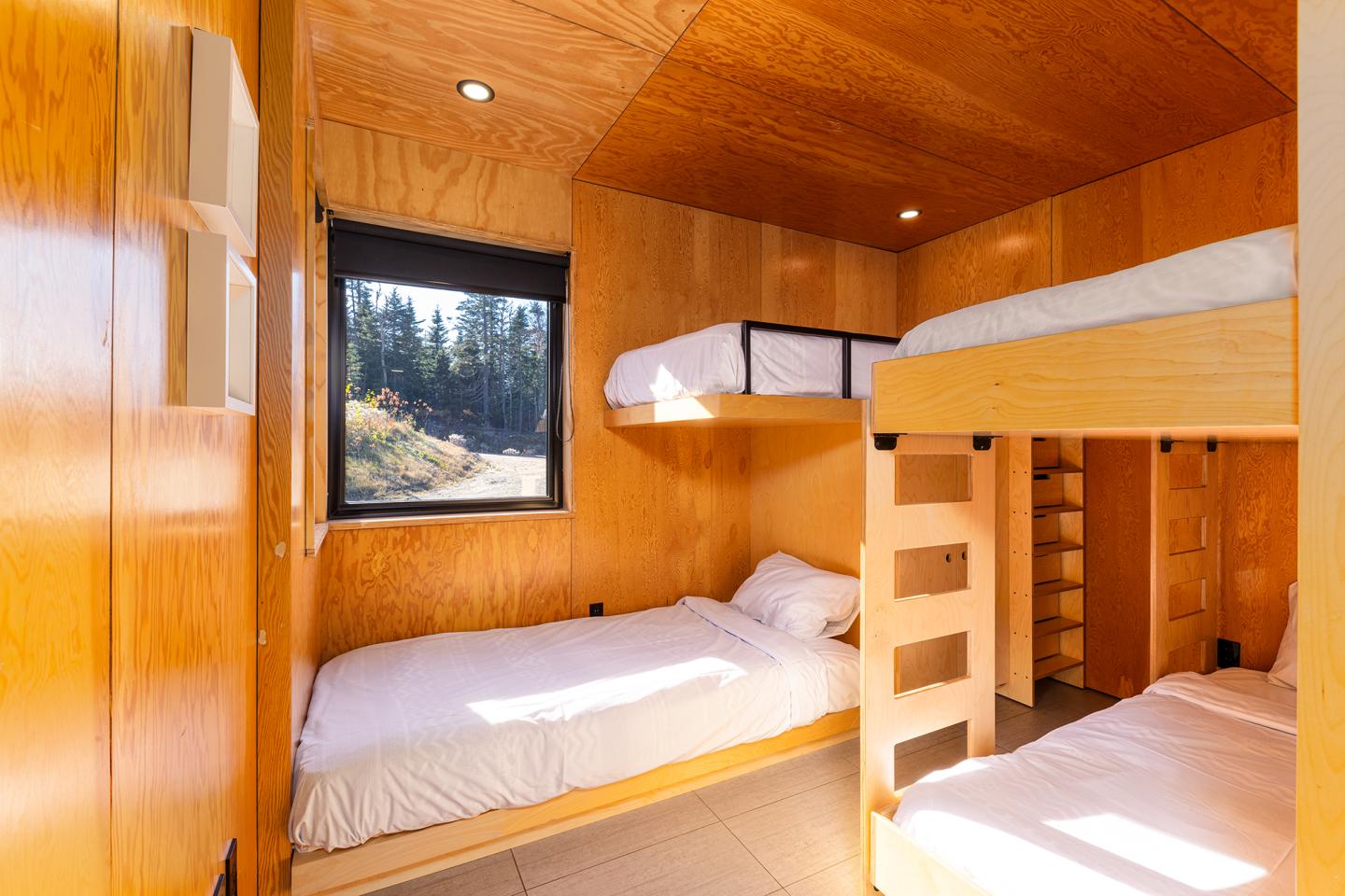 Chambre en bois avec un lit simple et des lits superposés, fenêtre donnant sur forêt.