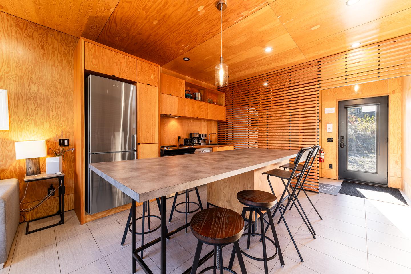 Cuisine moderne en bois avec îlot et tabourets, éclairage chaleureux.