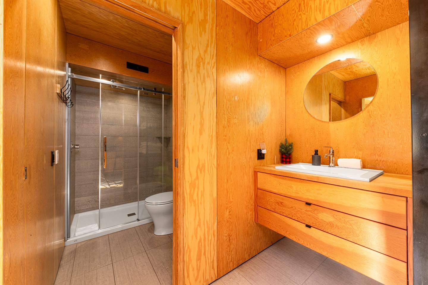 Salle de bain en bois avec douche, lavabo et miroir ovale.