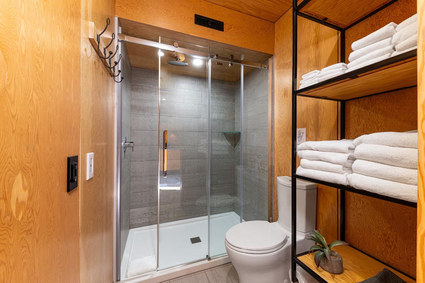 Salle de bain moderne avec douche en verre, toilettes et étagères avec serviettes.
