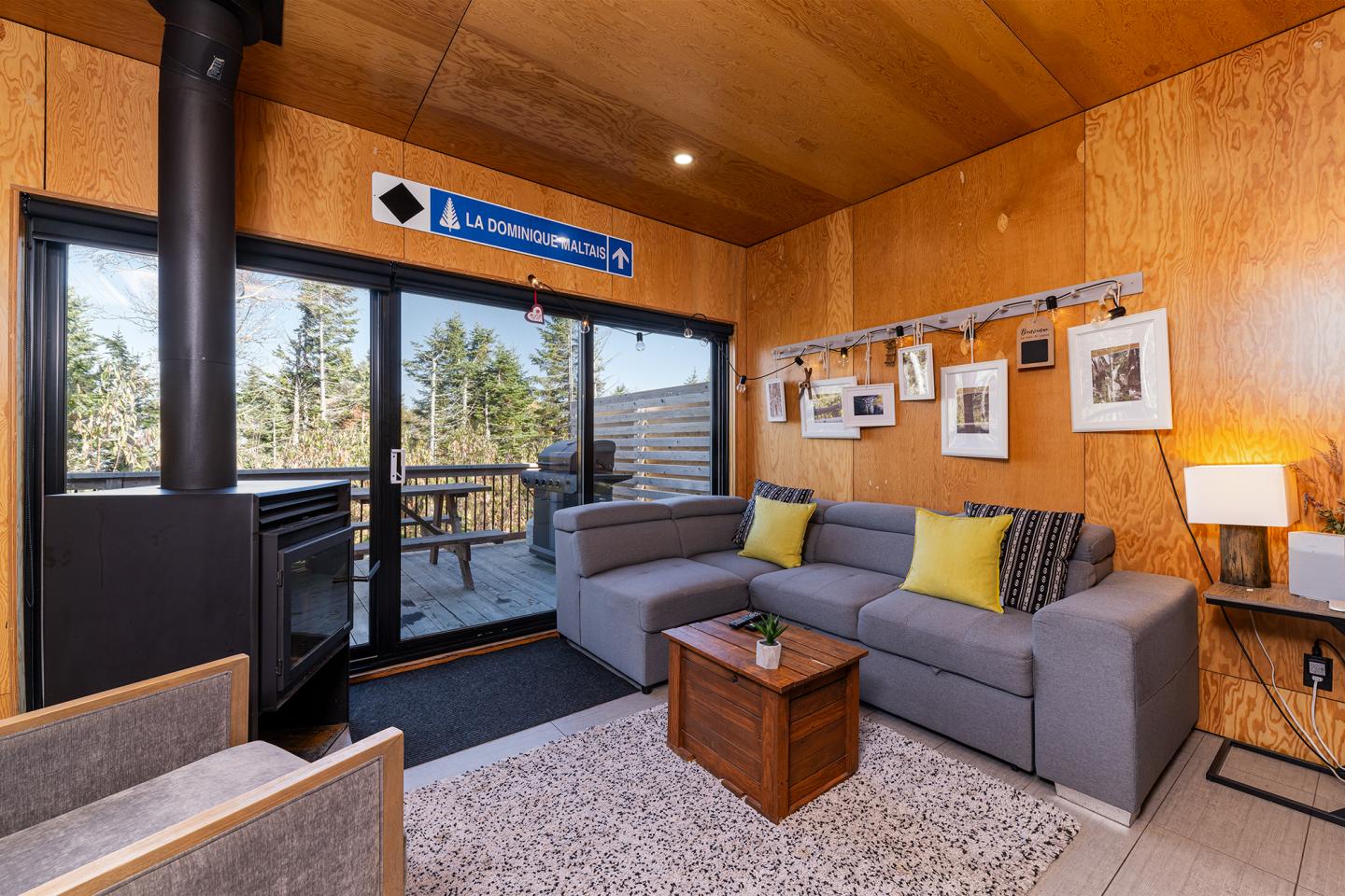 Salon moderne avec canapé gris, coussins jaunes, table basse en bois, cheminée, baies vitrées.