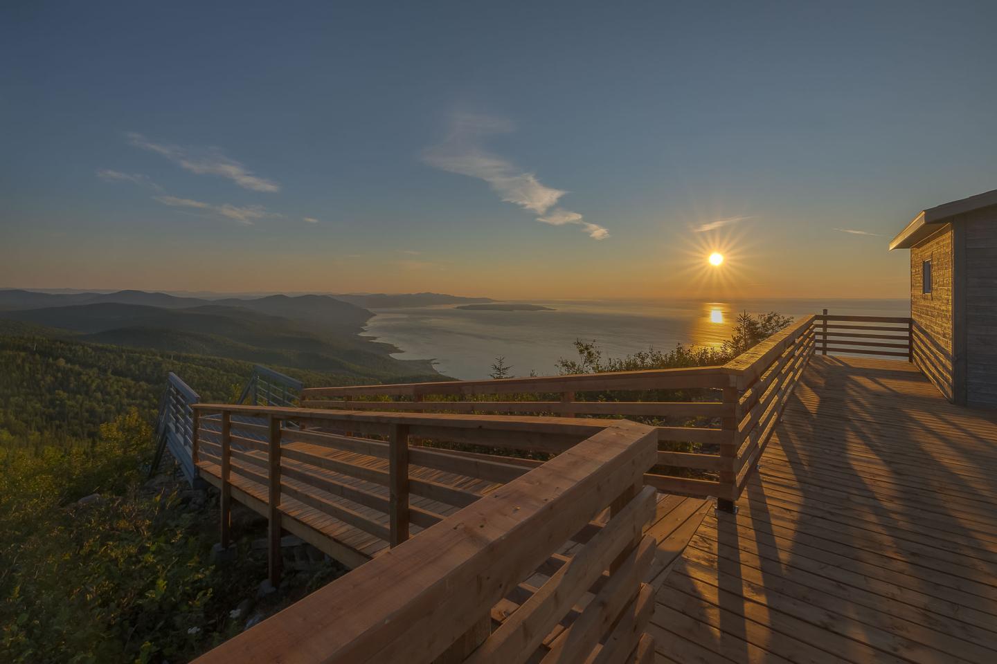 Terrasse en bois surplombant un paysage côtier au coucher du soleil.