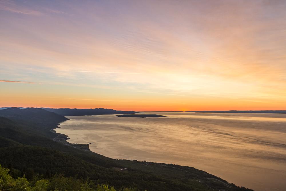 Coucher de soleil sur un lac bordé de collines sombres.