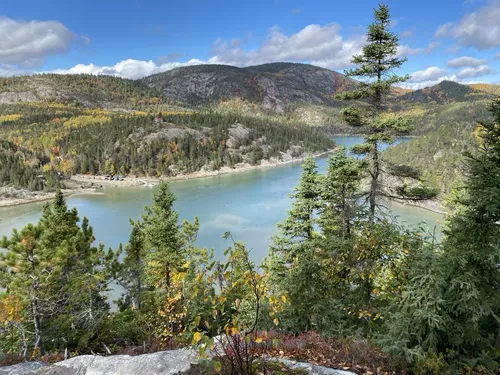 Paysage montagneux avec lac, arbres verts et ciel bleu.