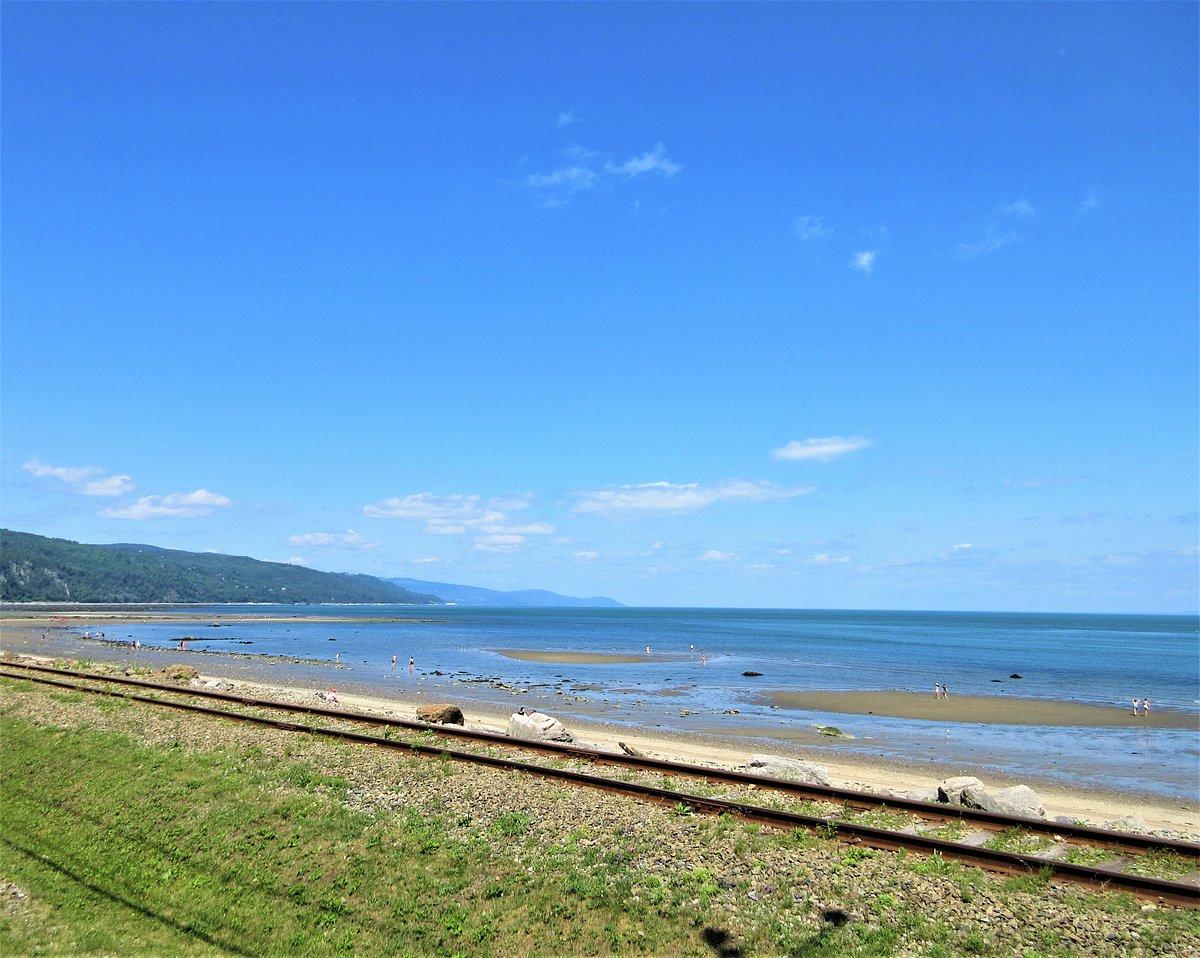 Plage avec voie ferrée, mer et ciel bleu.