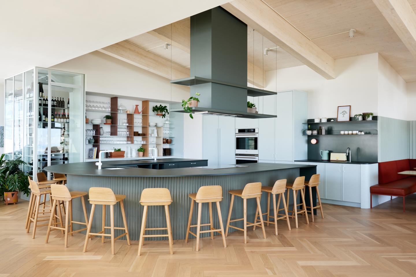 Cuisine moderne avec îlot central, tabourets en bois et étagères décorées.
